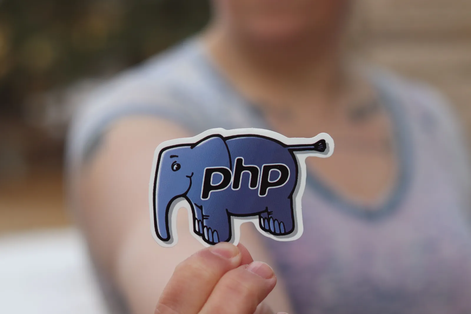 Hand holding up a blue PHP elephant logo sticker