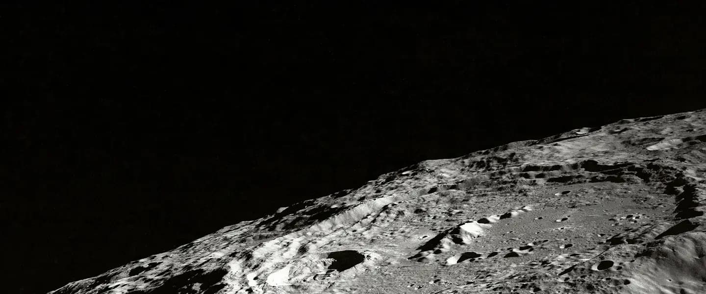 A black and white view of a cratered lunar surface sloping upward against the black void of space.